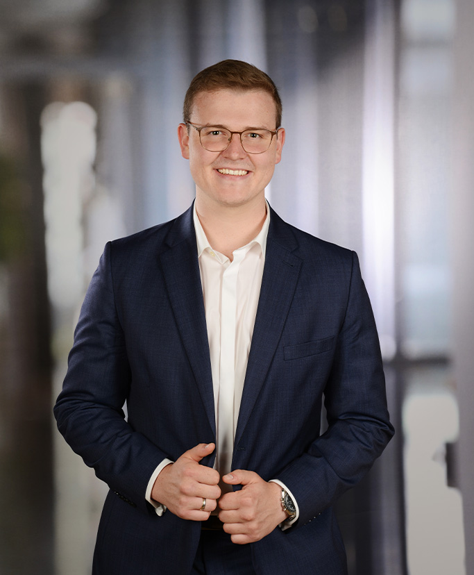Foto von Steuerberater Tim Eiselt im Anzug vor verschwommenem Hintergrund